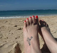 foot with tattoo of chicken on a beach